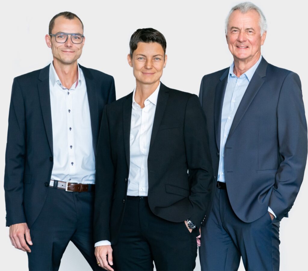 Drei Führungskräfte von Späh, rechts Thomas Späh, links Alfred Späh und Sandra Späh in der Mitte, posieren in schwarzen und blauen Anzügen vor einem hellen Hintergrund.