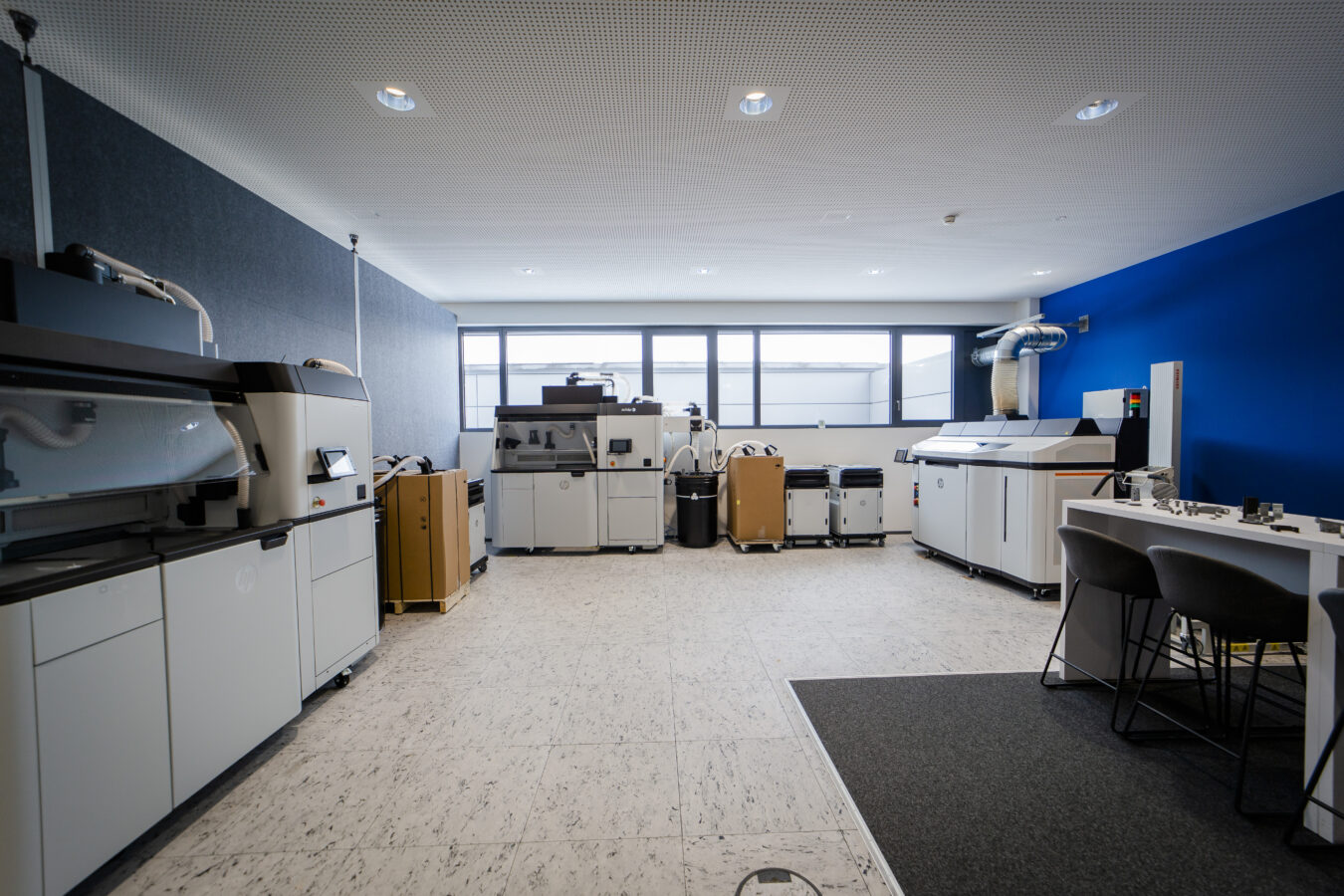 Das Bild zeigt einen sauberen, modernen Raum in der Firma Späh, der mit mehreren Industrie-3D-Druckern und zugehörigem Equipment für die additive Fertigung ausgestattet ist.