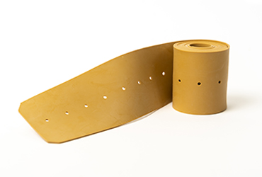 Ein langes, ockerfarbenes Gummiband mit regelmäßig gestanzten Löchern ist teilweise aufgerollt.