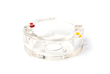 Ein transparentes, zylindrisches Kunststoffbauteil ist mit kleinen roten und gelben Markierungspunkten versehen.