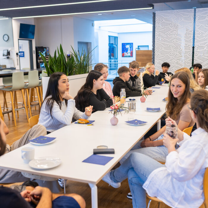 Alle Auszubildenden sitzen an einem Tisch in der Kantine um zu Frühstücken. 