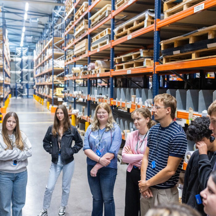 Eine Gruppe von Auszubildenden befinden sich im Lager der Firma Späh und hören aufmerksam zu wie ein Auszubildender über die Abteilung erzählt. 