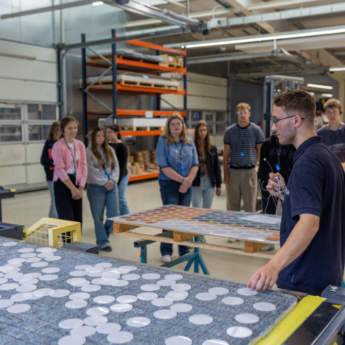 In der Produktionsabteilung ist eine Gruppe von Auszubildenden. Einer der Auszubildenden erklärt den anderen die Arbeitsprozesse und veranschaulicht diese anhand praktischer Beispiele.