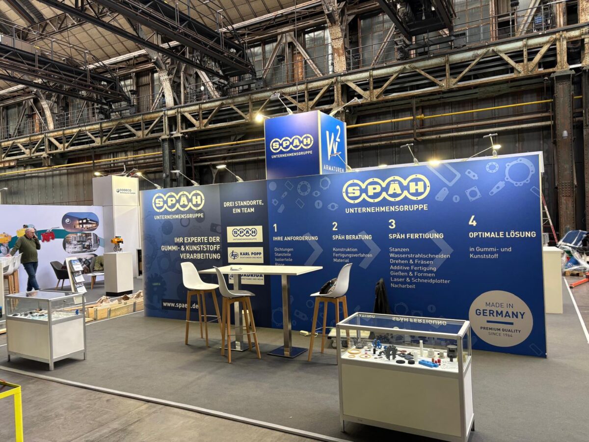 Ein Späh Messestand mit ausgestellten Teilen die von Späh gefertigt werden. Auf den Wänden sind Informationen über Späh. Auf der linken Seite ist ein Messestand eines anderen Unternehmens zu sehen. 