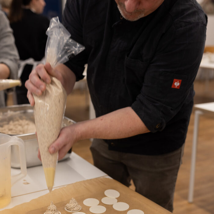Der Koch steht vor einem Backblech und gibt Spritzgebäck auf das Blech.