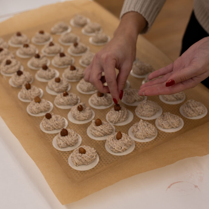 Eine Späh-Mitarbeiterin steht vor einem vollen Blech mit Weihnachtsgebäck und legt auf jedes Gebäck eine Haselnuss.