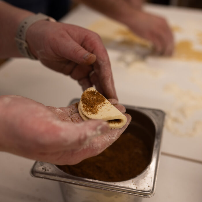 Zwei Späh-Mitarbeiter die zusammen Weihnachtsgebäck backen. Der eine Mitarbeiter sticht die Plätzchen aus. Der andere Mitarbeiter verziert diese Plätzchen.