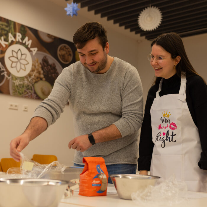 Zwei lächelnde Späh-Mitarbeiter in der Kantine beim Backen von Weihnachtsgebäck. Auf dem Tisch sind mehrere Schüsseln mit Zutaten.