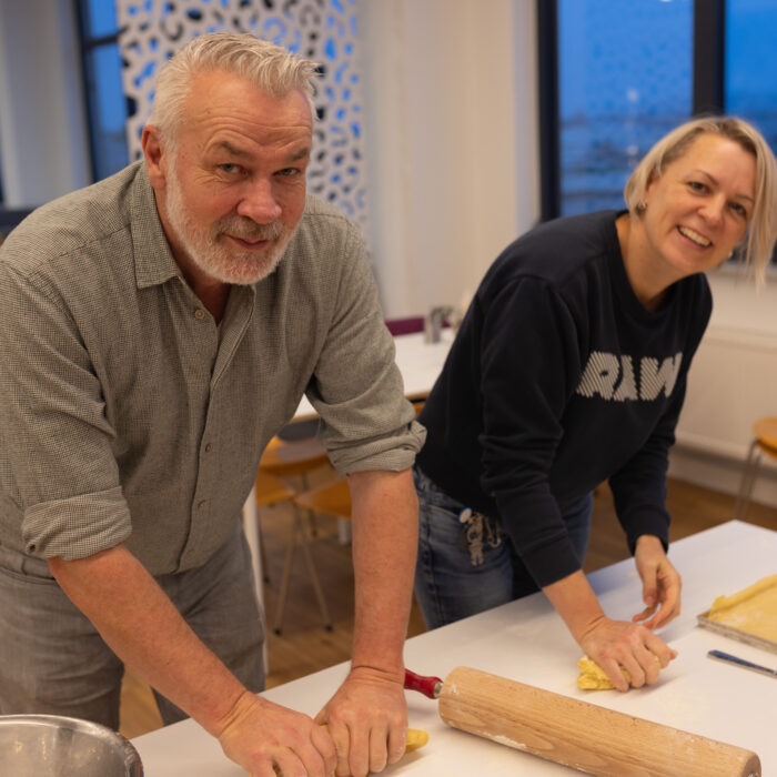 Zwei lächelnde Späh-Mitarbeiter in der Kantine haben Teig in ihrer Hand, den sie ausrollen müssen für das Ausstechen der Plätzchen.