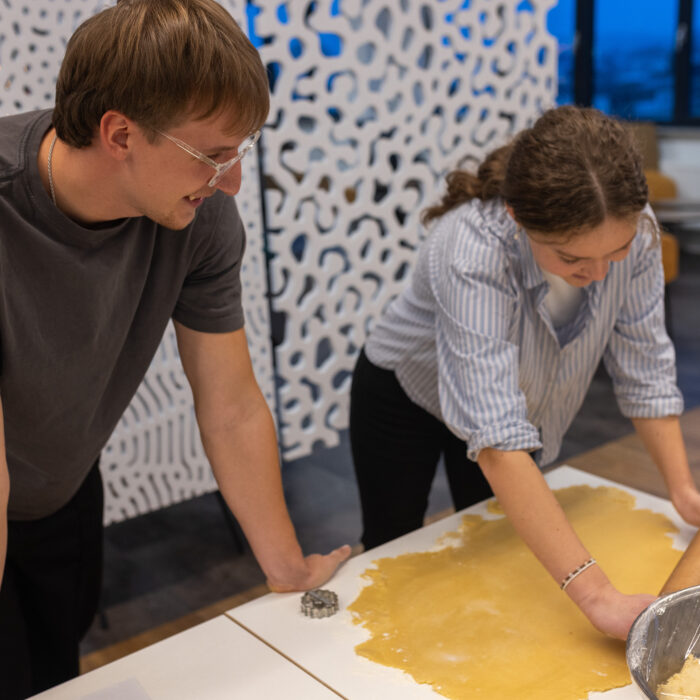 Zwei lächelnde Späh-Mitarbeiter rollen einen Teig aus um Plätzchen ausstechen zu können. In einer Schüssel befindet sich mehr Teig.